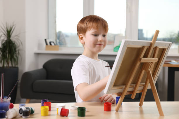 istock Little boy painting at table in studio. Using easel to hold canvas 1721256911