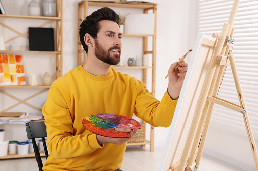 Man painting in studio. Using easel to hold canvas