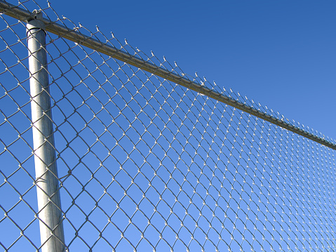 Cold steel chain-link fence with vivid blue sky behind.