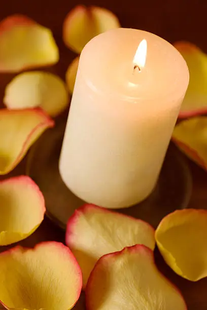 A burning candle and rose petals.  Shallow DOF with focus on the top of the candle