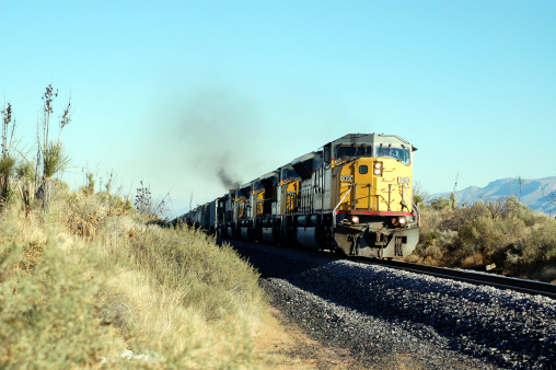 an american freight train with 4 engines on the way throughthe desert with the mountains in the background