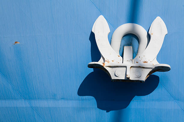 Ship's white anchor hoisted against a light blue hill stock photo