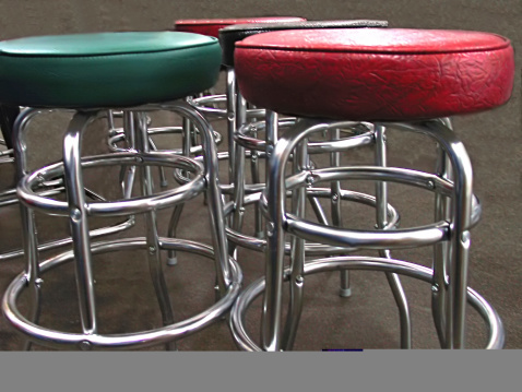 Padded seats and curved chrome legs on bar stools have retro styling.