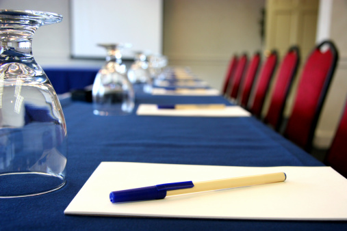 Business conference room with water glass, notepad, pens, chairs and a presentation screen. Room on notepad, screen, or pen for logo placement