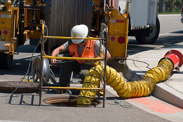 UTILITY WORKER A utility worker looks down a man-hole. manhole stock pictures, royalty-free photos & images