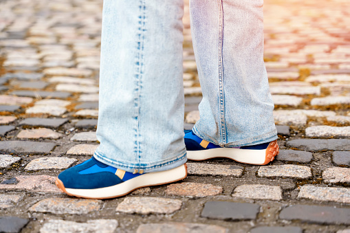 feet of a woman in jeans and a   sneakers  walking along a paved street  on the city street