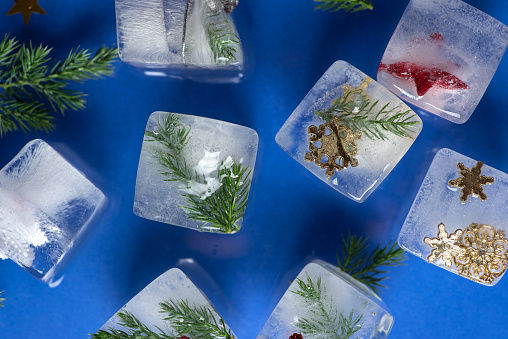 Studio shot of Christmas decorations frozen in ice cubes, over blue background