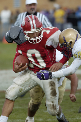 A high school american football player struggles for some hard fought yards.