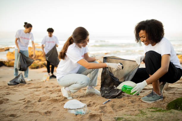 Positive young different people volunteers in gloves with garbage bags clean up trash on sea beach Positive young different people volunteers in gloves with garbage bags clean up trash on sea beach, outdoor. Ocean pollution and environment conservation, protecting planet, Earth day earth day clean up stock pictures, royalty-free photos & images