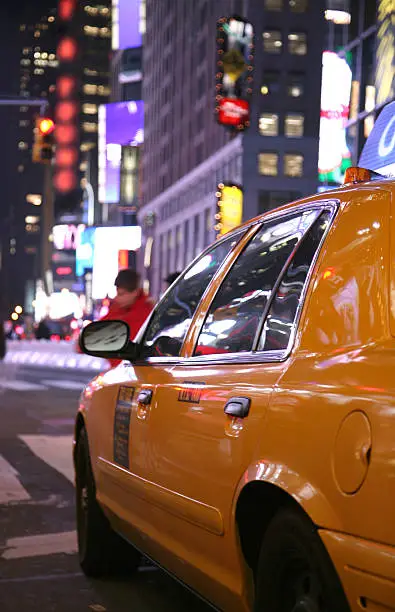 Neon lights reflect on side of taxicab at night in Times Square, New York City, New York, USA.