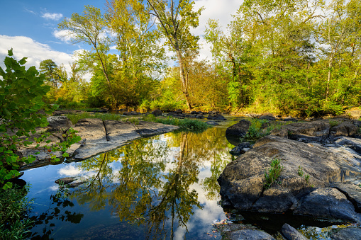 A rocky landscape on the beautiful Haw River at sundown with leafy trees reflecting in the water in North Carolina in the Eastern U.S.