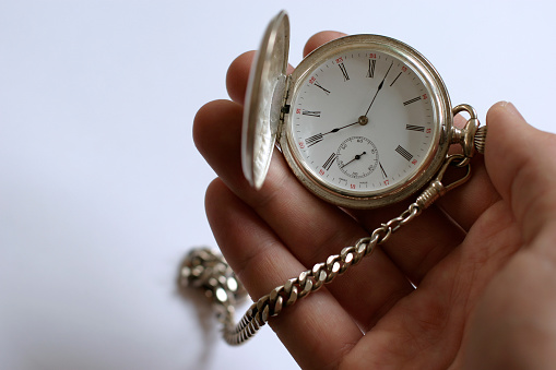 Hand holding a silver clock. Focus on the clock.