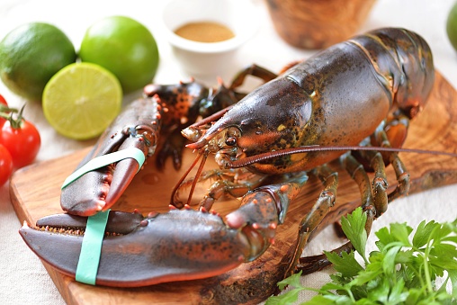 Raw fresh lobster on a cutting board with lime and spices.