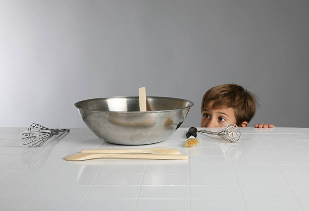 Boy Peaks Over Counter Young boy peaks over a counter at a silver bowl. Viewer only sees hs eys and top of head. kid peaking over counter stock pictures, royalty-free photos & images