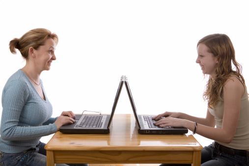 Mother and daughter sitting in front of each other with laptop computers. Isolated on white.
