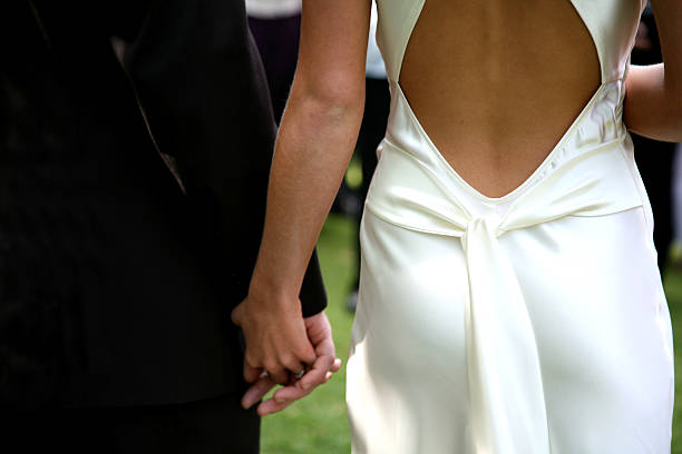 Dressed-up couple holding hands walking to the aisle bride and groom holding hands during marriage ceremony man touching womans buttock stock pictures, royalty-free photos & images