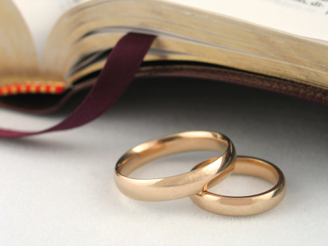 Gold wedding bands placed in front of a Bible. Shallow depth of field with only a portion of the rings in sharp focus.