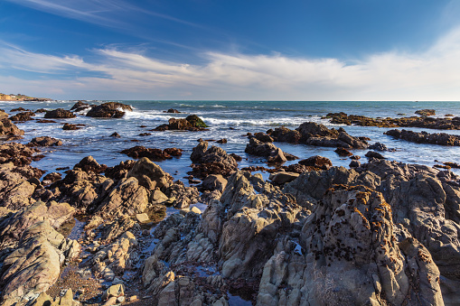 Rocky beach at low tide in Cambria, California. Pacific Ocean beyond. Blue sky, clouds in background.