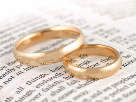 Gold wedding bands placed on a King James Version Bible. The passage is 1 Corinthians 13 (the love chapter).Shallow depth of field with only a portion of the rings and words in sharp focus.