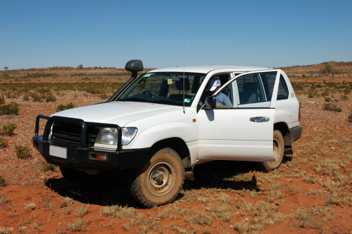 A four wheel drive offroad in the outback.  White vehicle, red dirt, right hand drive vehicle.