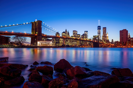 Queensboro Bridge and Midtown Manhattan shot from Roosevelt Island. An empty bench sits in the foreground with cherry blossoms overhead