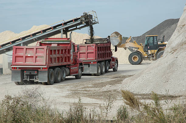 Conveyor Belt Loading Dump Trucks At Road Construction Site A red dump truck is loaded by a conveyor system with sifted crushed concrete for use in a freeway expansion project in east Texas as a second red dump truck is in line behind it.  A front-end loader is passing in the background and piles of the road material are all around. dump truck photos stock pictures, royalty-free photos & images