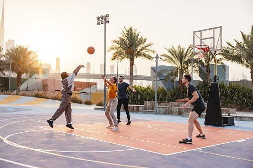 Young Adult Middle Eastern  Shooting A Ball Toward A Basket Outside. She Is Playing With A Group Of Friends In Dubai.