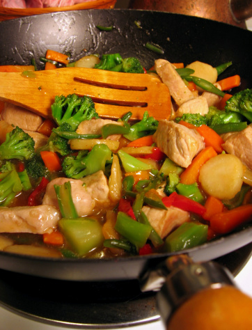 A pan filled with Chinese stir-fry and a wooden spoon.  The shot is a macro with a very shallow depth of field such that only the food in the center of the pan is in focus.
