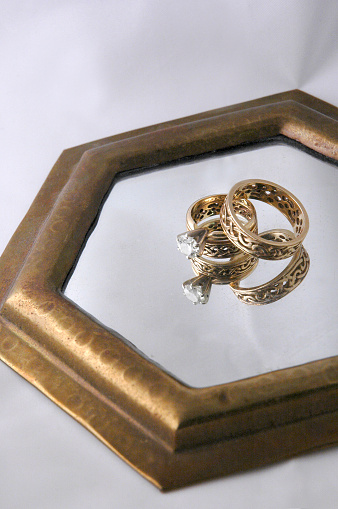 Gold celtic wedding rings placed together on a reflective mirror with a white background.
