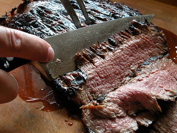 Close-up of a knife carving a piece of grilled flank stake stock photo