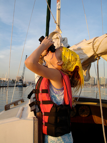 Young girl looks up with binoculars on sailboat