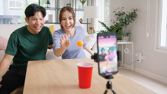 Adult influencer youtuber asia people vlogger record viral video vlog page live fun game beer ping pong ball throw cup on IG reel instagram tiktok social media trendy joy side hustle for young couple.