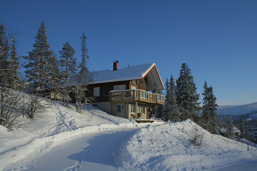A traditional wooden chalet surrounded by deep snow on a blue sky day.