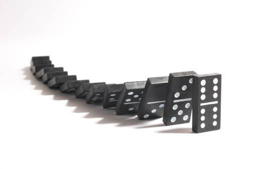 Stack of dominoes fall toward camera on white background.