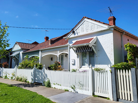 Melbourne, Australia: September 22, 2023: Row of detached bungalow homes in the residential suburb of St Kilda in Melbourne. Traditionally built bungalows in the 20th century Australian style with a porch, ornate verandah and garden gate with white picket fence and a blue sky background.