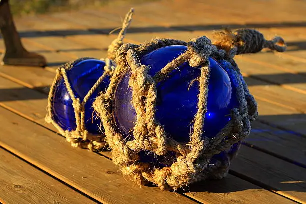 Two blue glass spheres resting on wooden boards. These balls where originally used by fishermen. In modern times used as decorations inside and outside.