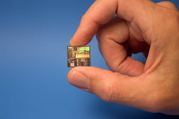 Computer Chip Microprocesser die held between the fingers on a blue background. gchutka stock pictures, royalty-free photos & images