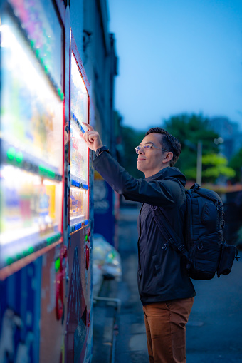 Hispanic tourist male with backpack buying snack in vending machine on street in evening in Tokyo, Japan