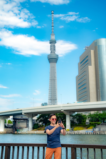 Hispanic male tourist traveler using smartphone near Tokyo Skytree observation tower under blue sky, Japan