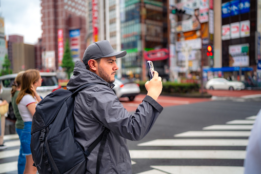 Hispanic male tourist in warm clothes taking photo on standing in Akihabara neighborhood in Tokyo, Japan