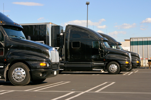 Three black 18 wheelers ready for freight distribution; Identical Black Truck Cabs used for Freight Transportation in day, sunlight,side view,nobody,new trucks, 18 wheelers, three trucks