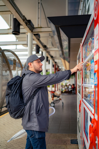 Hispanic male tourist in jacket buying snack in vending machine near Odaiba during trip in Tokyo Japan