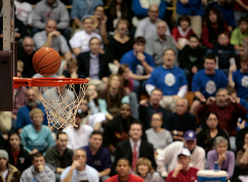 A basketball bounces on the rim with out of focus fans in the background.