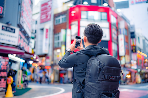 Hispanic male tourist taking picture on smartphone in Shinjuku street of Tokyo city, Japan