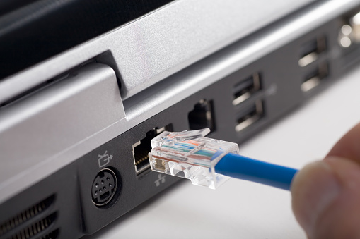 closeup image of hand plugging ethernet cable into laptop