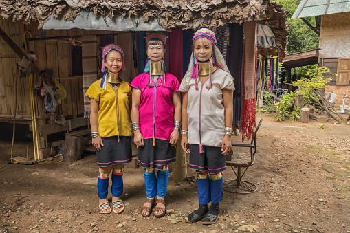 portrait of three long-necked Karen women with brass neck rings wearing traditional vibrant Karen style dress standing in their rustic village at Pai in Mae Hong Son, Thailand