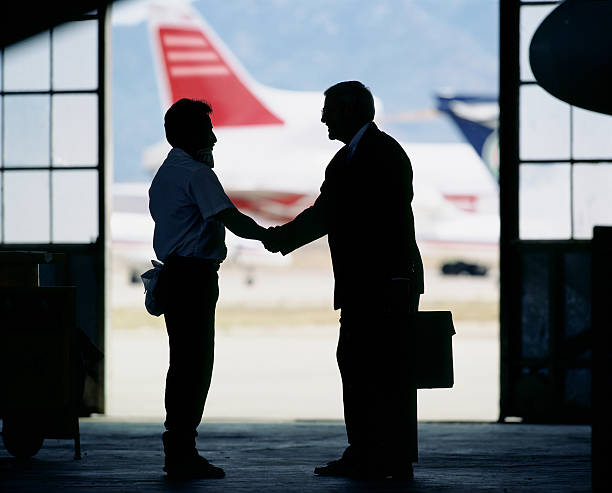 Silhouette of men shaking hands in airport hangar stock photo