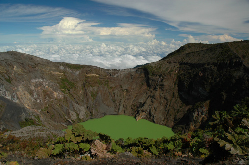 Vivid green crater lake inside Irazu Volcano in Costa Rica with dramatic cloudscape - Irazu National Park.