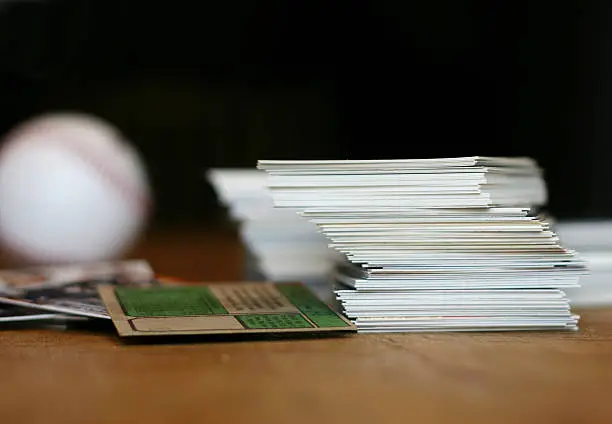 "Collection of baseball cards and baseball on old wooden table.  Shallow dof, focus on stack of cards baseball in background is out of focus."