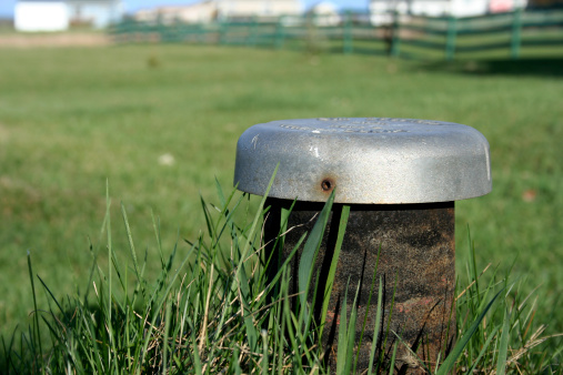 A septic tank pipe peeks out from a beautiful lawn on a spring day.Focus on the foreground.